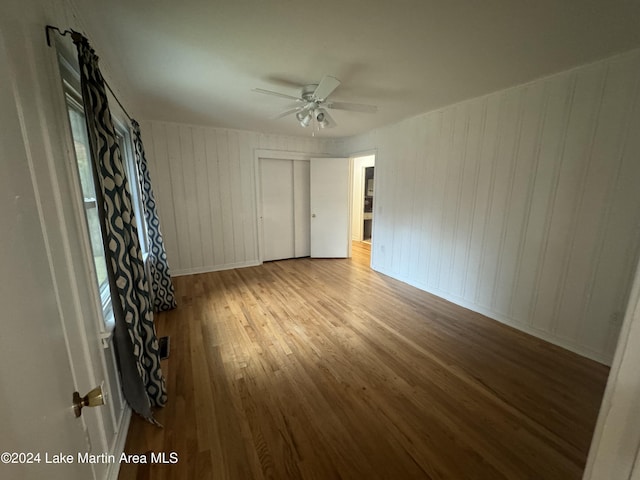 unfurnished room with ceiling fan, wooden walls, and light wood-type flooring