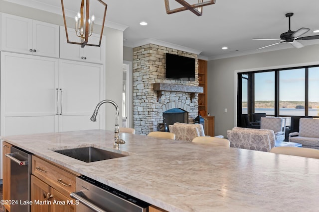 kitchen featuring dishwasher, sink, a stone fireplace, decorative light fixtures, and ornamental molding