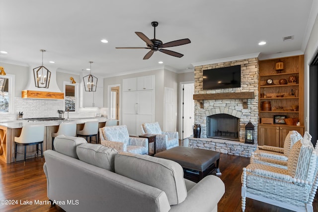 living room with ceiling fan, crown molding, dark wood-type flooring, and a stone fireplace