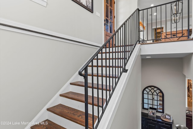 staircase with wood-type flooring and a towering ceiling