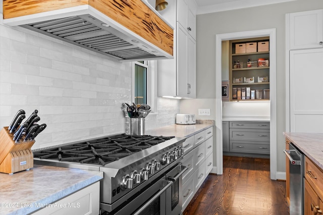 kitchen with white cabinetry, stainless steel appliances, dark hardwood / wood-style flooring, backsplash, and wall chimney exhaust hood