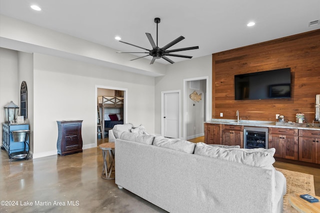 living room featuring ceiling fan, concrete floors, wet bar, wood walls, and wine cooler