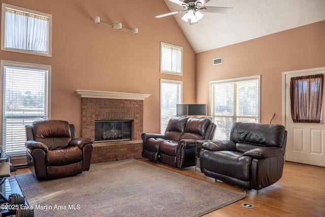 living room with ceiling fan, a brick fireplace, plenty of natural light, and light hardwood / wood-style flooring