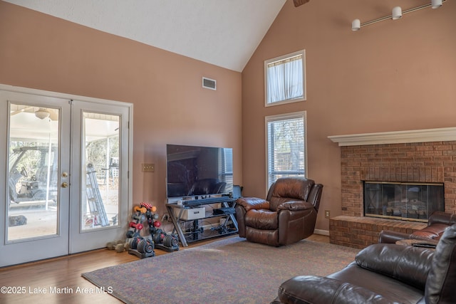 living room featuring a brick fireplace, light hardwood / wood-style flooring, french doors, and high vaulted ceiling