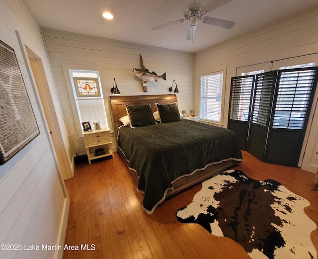 bedroom featuring hardwood / wood-style floors, ceiling fan, and wood walls