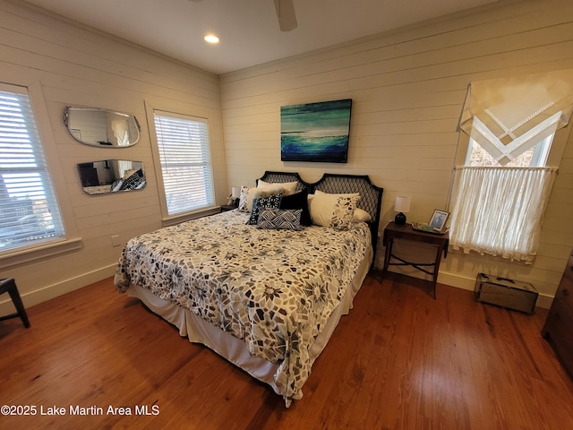 bedroom with ceiling fan, wood-type flooring, multiple windows, and wood walls