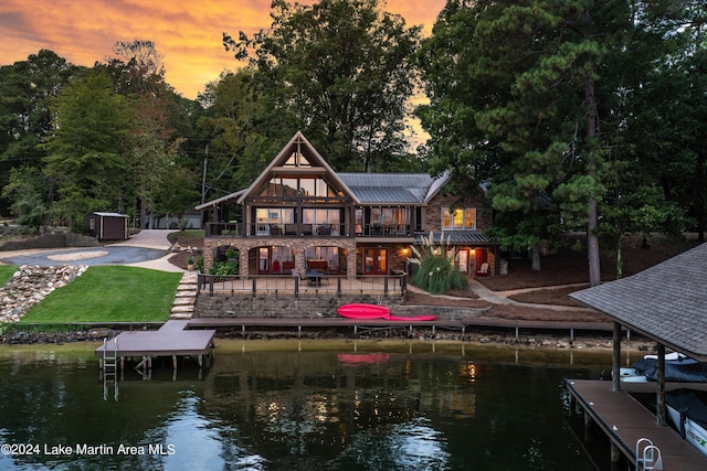 back house at dusk with a water view, a yard, and a balcony