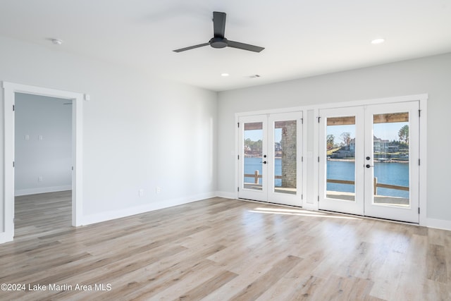 spare room with ceiling fan, a water view, light wood-type flooring, and french doors