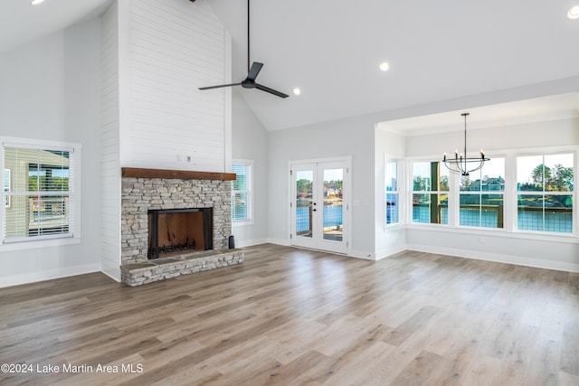 unfurnished living room with high vaulted ceiling, ceiling fan with notable chandelier, a water view, a fireplace, and wood-type flooring