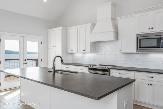 kitchen with premium range hood, stainless steel appliances, a kitchen island with sink, sink, and a water view