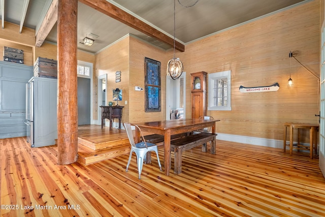 dining area featuring an inviting chandelier, beam ceiling, wooden walls, and light hardwood / wood-style floors