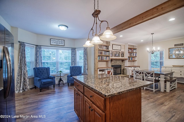 kitchen with hanging light fixtures, black fridge, dark hardwood / wood-style floors, dark stone countertops, and a fireplace