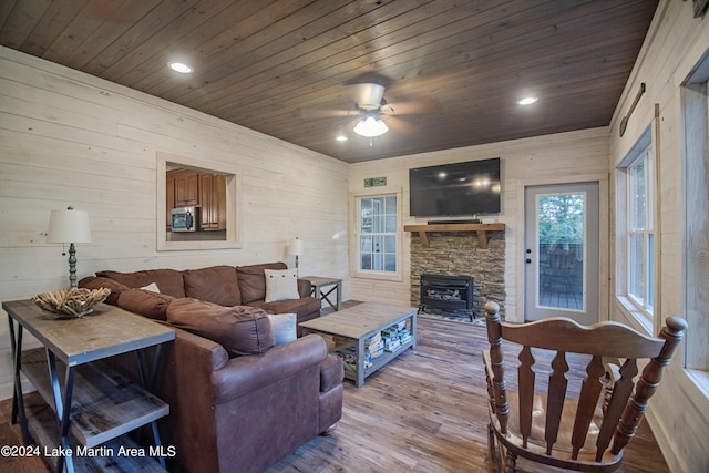 living room featuring wooden ceiling, ceiling fan, a wood stove, and light hardwood / wood-style flooring