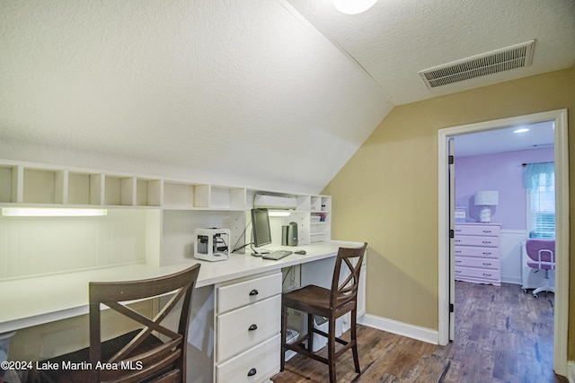 office featuring a textured ceiling, vaulted ceiling, dark wood-type flooring, built in desk, and an AC wall unit