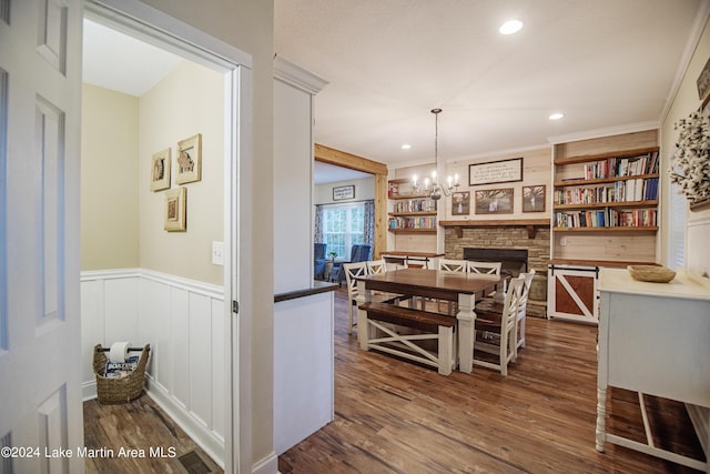 dining area with a stone fireplace, crown molding, dark hardwood / wood-style floors, built in shelves, and a notable chandelier