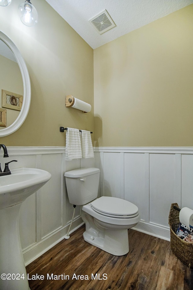 bathroom with wood-type flooring, a textured ceiling, toilet, and sink