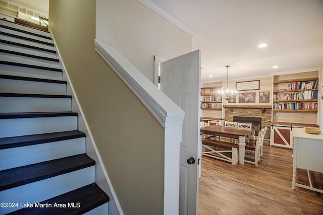 stairway featuring hardwood / wood-style floors, an inviting chandelier, built in shelves, ornamental molding, and a fireplace