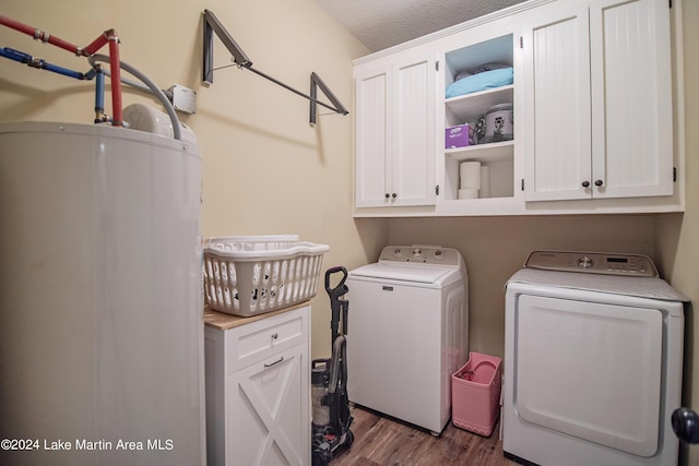 clothes washing area featuring washing machine and clothes dryer, cabinets, gas water heater, dark wood-type flooring, and a textured ceiling