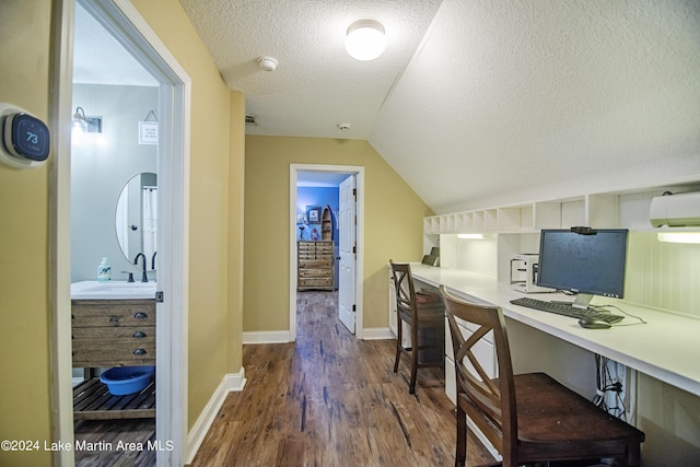 office area featuring lofted ceiling, dark wood-type flooring, sink, built in desk, and a textured ceiling