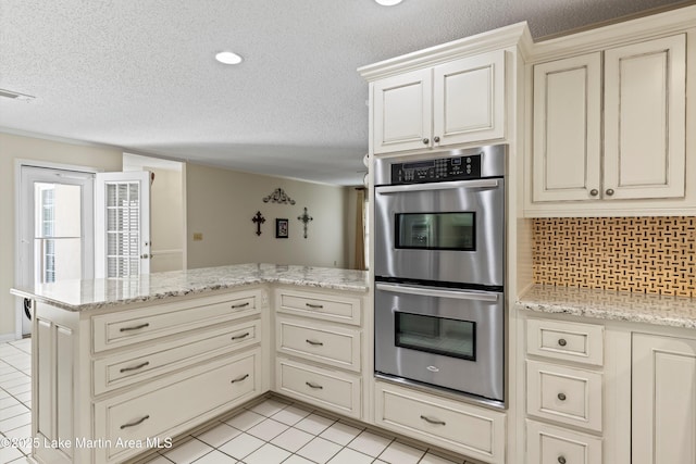 970 Raintree Dr, Alexander City, AL 35010 - kitchen with double oven, cream cabinets, a peninsula, a textured ceiling, and light tile patterned floors