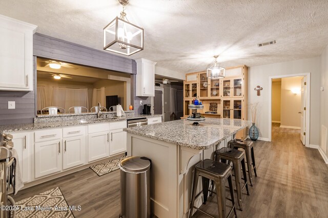 kitchen with white cabinets, hardwood / wood-style floors, a center island, and decorative light fixtures