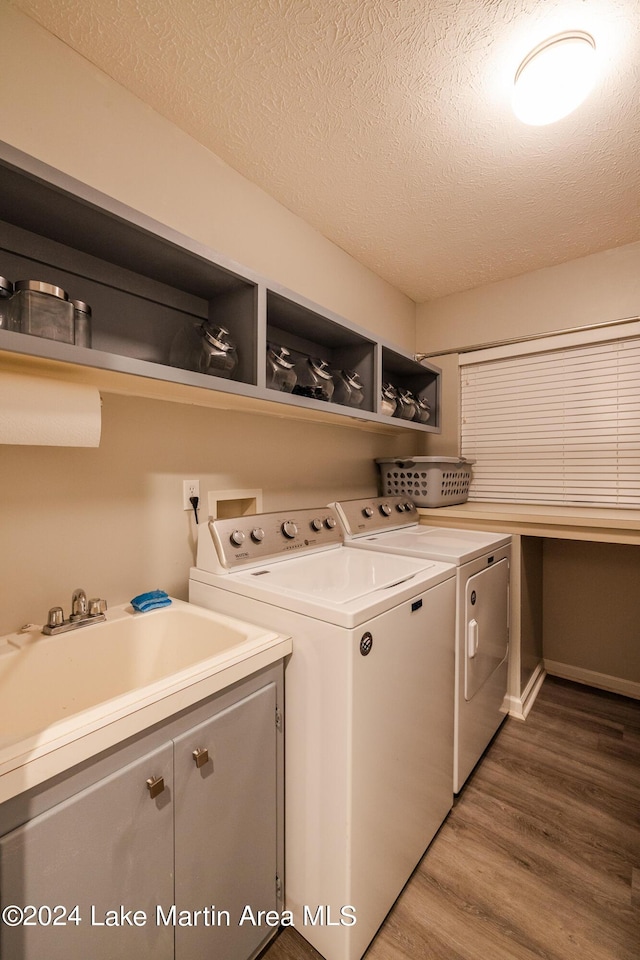 washroom with cabinets, sink, hardwood / wood-style flooring, independent washer and dryer, and a textured ceiling