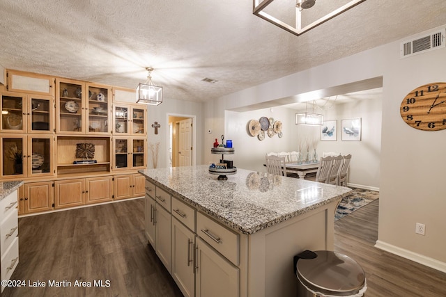 kitchen with pendant lighting, dark hardwood / wood-style floors, a textured ceiling, a kitchen island, and light stone counters