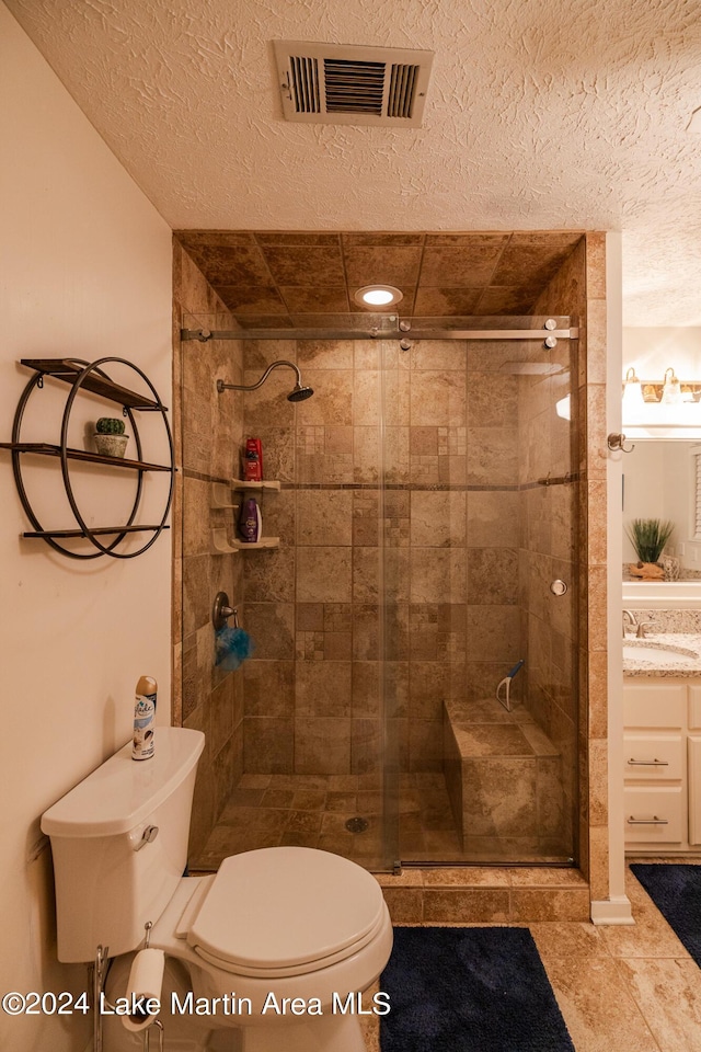 bathroom featuring tile patterned floors, a textured ceiling, vanity, a shower with door, and toilet