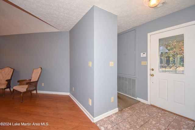 entryway with a textured ceiling, light hardwood / wood-style flooring, and lofted ceiling