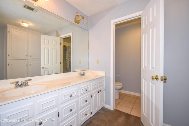 bathroom featuring tile patterned flooring, vanity, a textured ceiling, and toilet