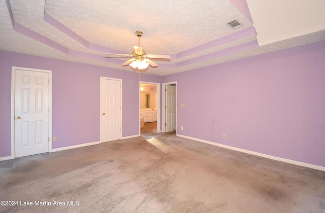 unfurnished bedroom featuring ceiling fan, carpet floors, ensuite bathroom, and a tray ceiling