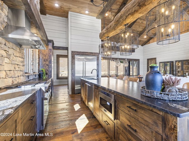 kitchen featuring dark stone counters, premium appliances, dark wood-type flooring, wall chimney range hood, and high vaulted ceiling