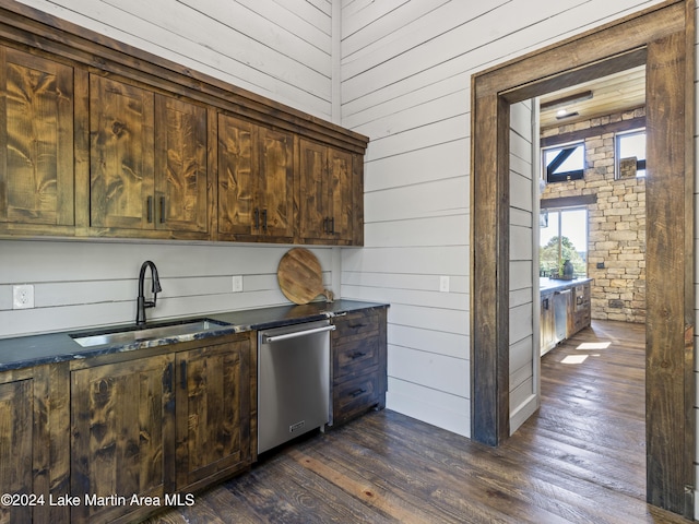 kitchen featuring wood walls, sink, dark wood-type flooring, and stainless steel dishwasher