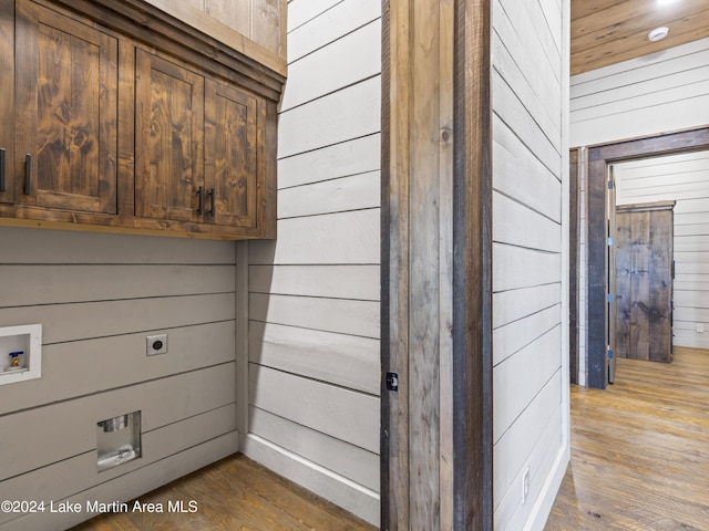 laundry room with cabinets, hookup for a washing machine, light wood-type flooring, and wooden walls