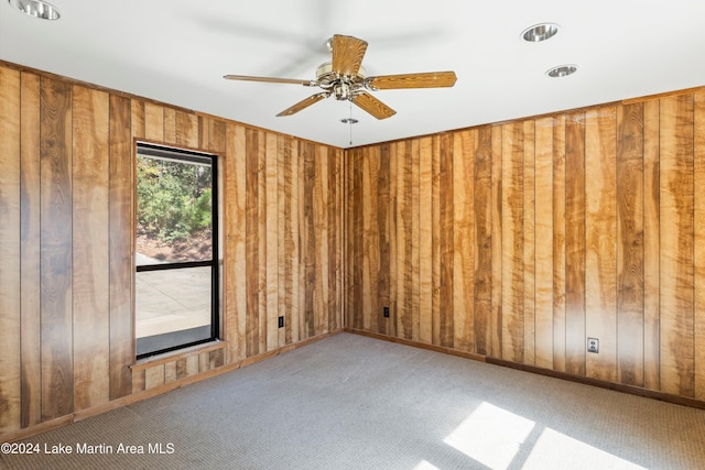 carpeted spare room with baseboards, wood walls, and ceiling fan