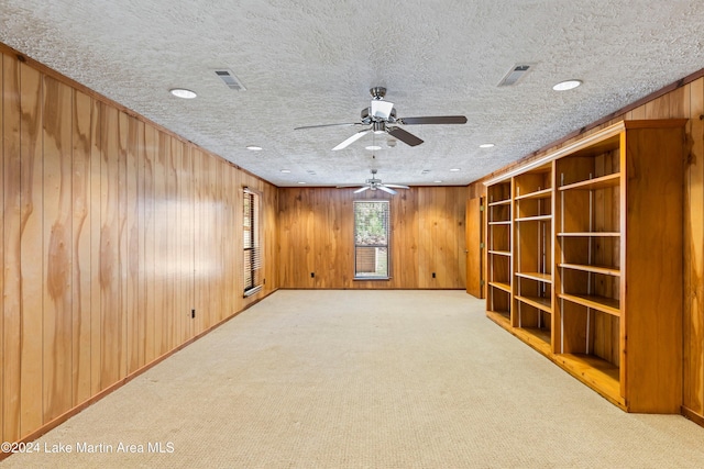 unfurnished room with visible vents, light carpet, a ceiling fan, a textured ceiling, and wooden walls