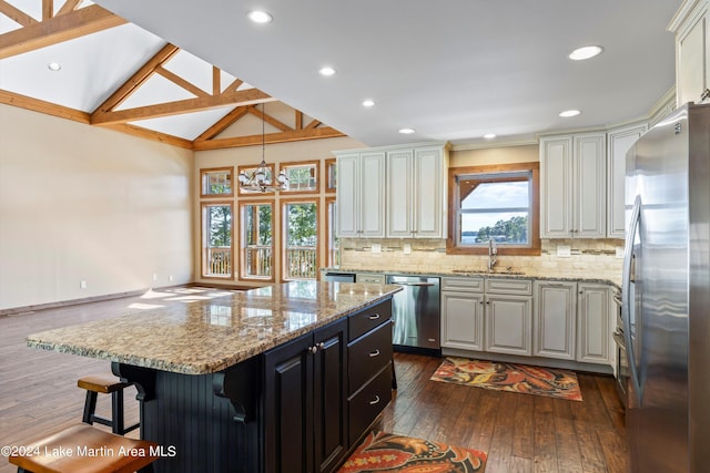 kitchen with lofted ceiling, a sink, stainless steel appliances, backsplash, and a center island