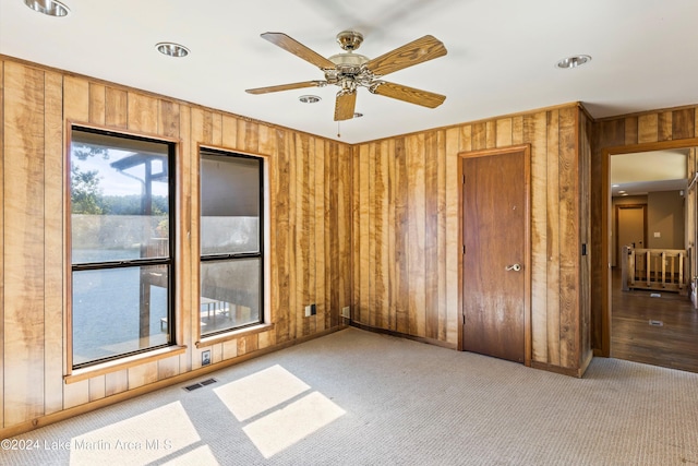 carpeted empty room with a ceiling fan, visible vents, and wood walls