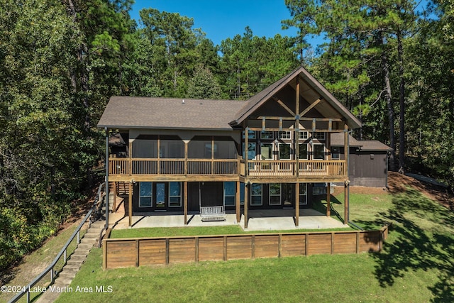 back of house with a wooden deck, roof with shingles, a lawn, a sunroom, and a patio