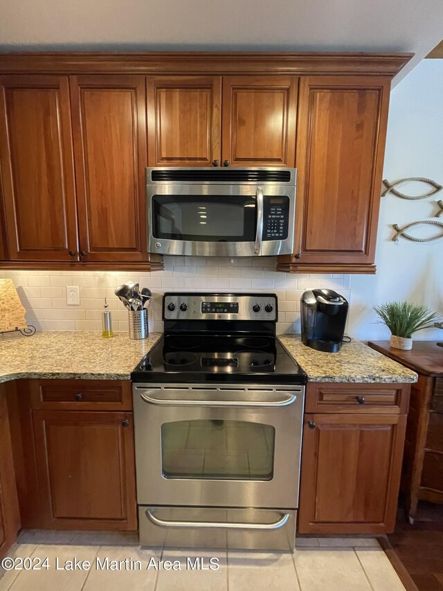 kitchen featuring light stone countertops, stainless steel appliances, light tile patterned floors, and tasteful backsplash