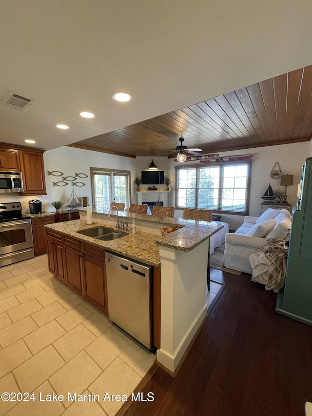 kitchen featuring wooden ceiling, sink, an island with sink, light stone counters, and stainless steel appliances