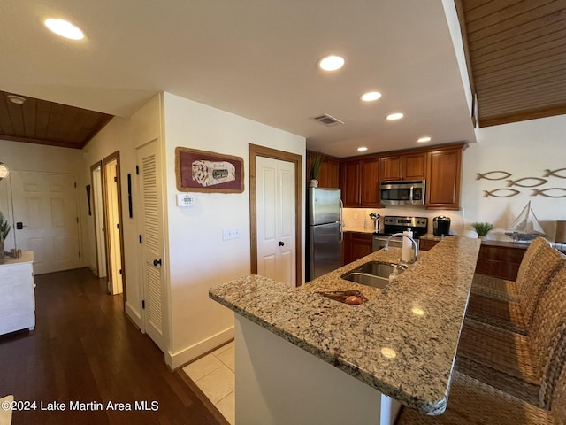 kitchen featuring light stone countertops, appliances with stainless steel finishes, sink, hardwood / wood-style flooring, and a breakfast bar area