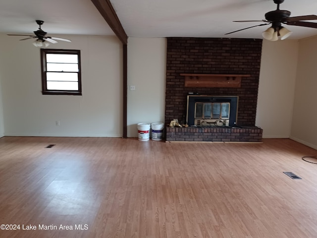 unfurnished living room with ceiling fan, a fireplace, beamed ceiling, and hardwood / wood-style flooring