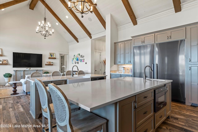 kitchen with built in microwave, hanging light fixtures, an inviting chandelier, high vaulted ceiling, and a large island with sink