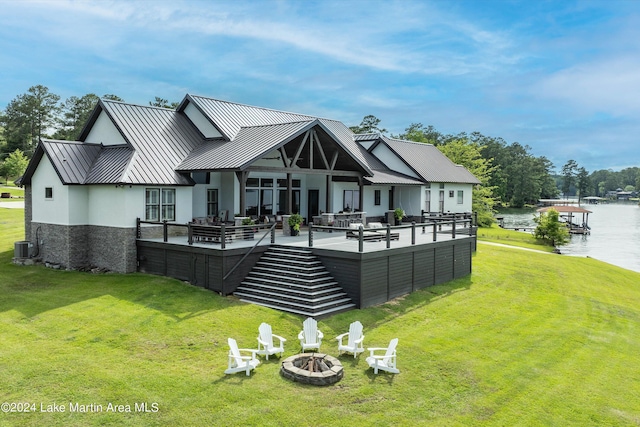 rear view of house featuring a deck with water view, an outdoor living space with a fire pit, a lawn, and central air condition unit