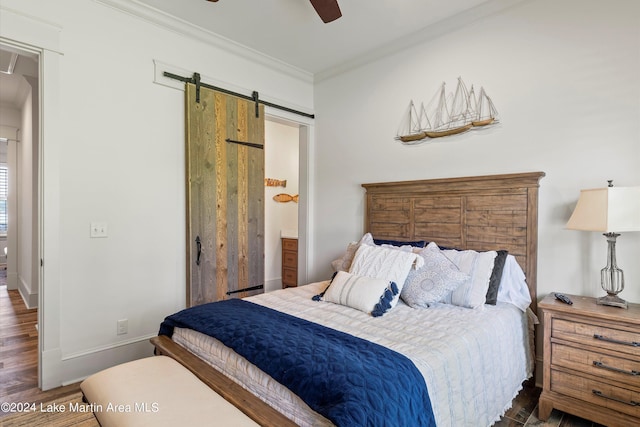 bedroom featuring a barn door, dark hardwood / wood-style floors, ceiling fan, and ornamental molding