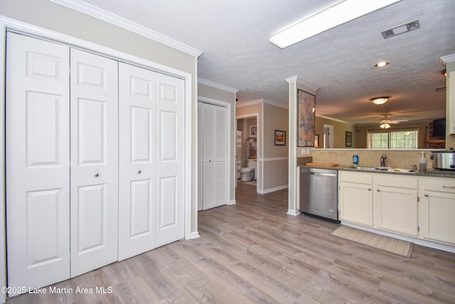 kitchen featuring a sink, light wood-style floors, dishwasher, backsplash, and visible vents