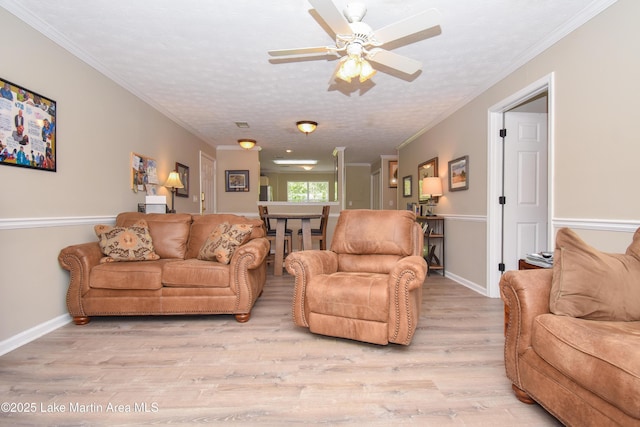 living room with light wood-style floors, ornamental molding, baseboards, and ceiling fan