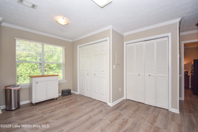 unfurnished bedroom featuring visible vents, crown molding, baseboards, two closets, and light wood-style flooring