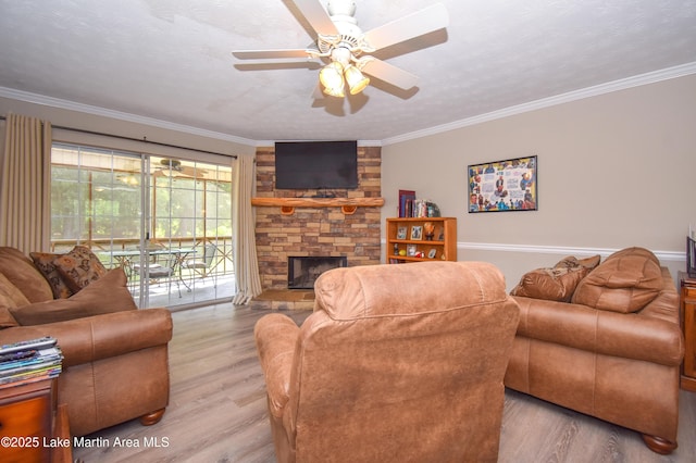 living area featuring ceiling fan, ornamental molding, wood finished floors, and a stone fireplace